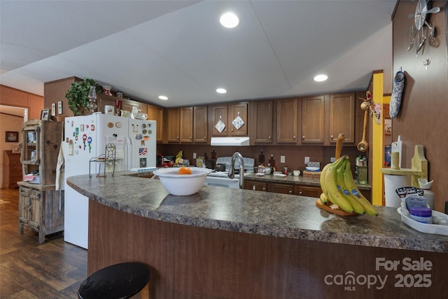 kitchen with dark hardwood / wood-style flooring, white appliances, and kitchen peninsula