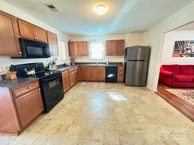 kitchen with visible vents, brown cabinetry, dark countertops, black appliances, and a sink