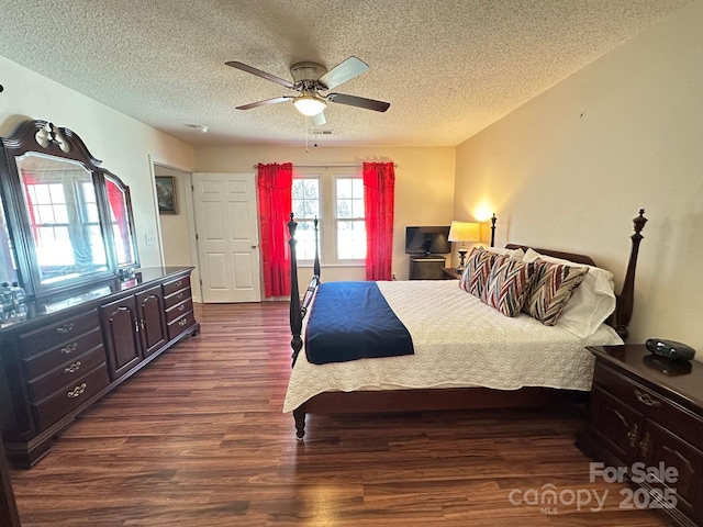 bedroom with ceiling fan, a textured ceiling, visible vents, and dark wood-style flooring