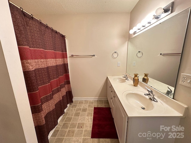 bathroom featuring a sink, a textured ceiling, baseboards, and double vanity