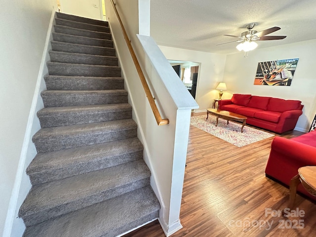 staircase featuring a ceiling fan, a textured ceiling, baseboards, and wood finished floors