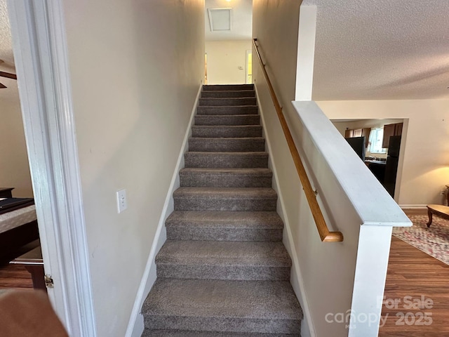 staircase featuring baseboards, a textured ceiling, and wood finished floors