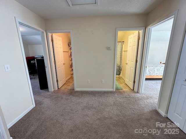 unfurnished bedroom with a spacious closet, attic access, light carpet, a textured ceiling, and baseboards