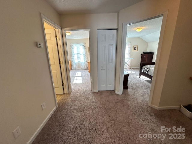 hall with light carpet, a textured ceiling, and baseboards