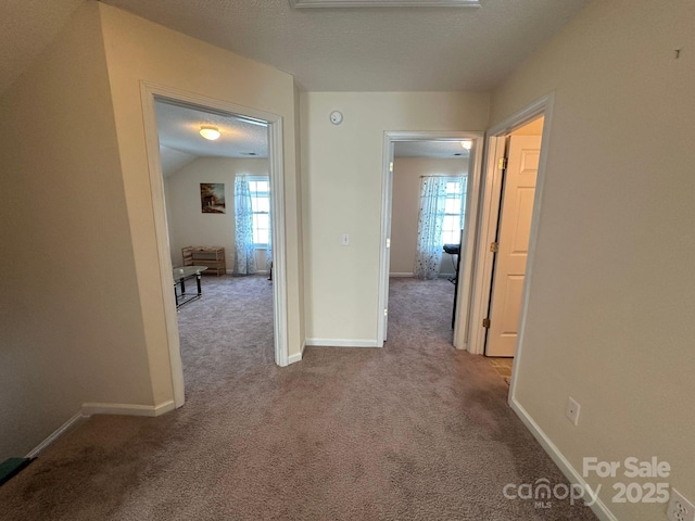 hall featuring a healthy amount of sunlight, baseboards, and light colored carpet