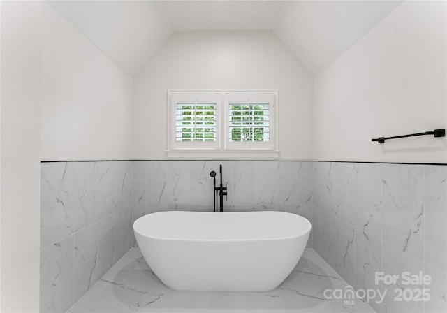 2809 Glendale Rd, Charlotte, NC 28209 - bathroom featuring marble tiled floors, a freestanding tub, tile walls, wainscoting, and vaulted ceiling