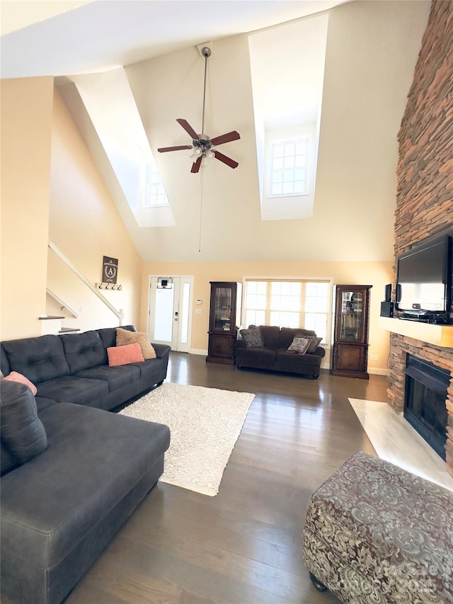 living room with ceiling fan, a skylight, high vaulted ceiling, dark hardwood / wood-style flooring, and a stone fireplace