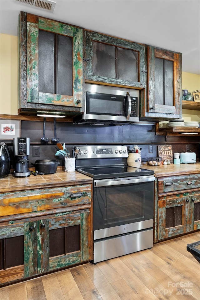 kitchen with stainless steel appliances, dark brown cabinets, and light wood-type flooring