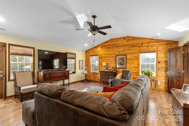 living room featuring vaulted ceiling, light hardwood / wood-style floors, ceiling fan, and wood walls