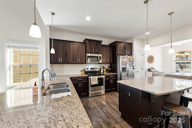 kitchen with sink, appliances with stainless steel finishes, hanging light fixtures, light stone countertops, and a kitchen bar