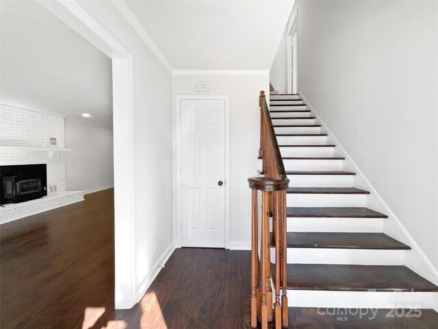 staircase with ornamental molding, wood-type flooring, and a brick fireplace