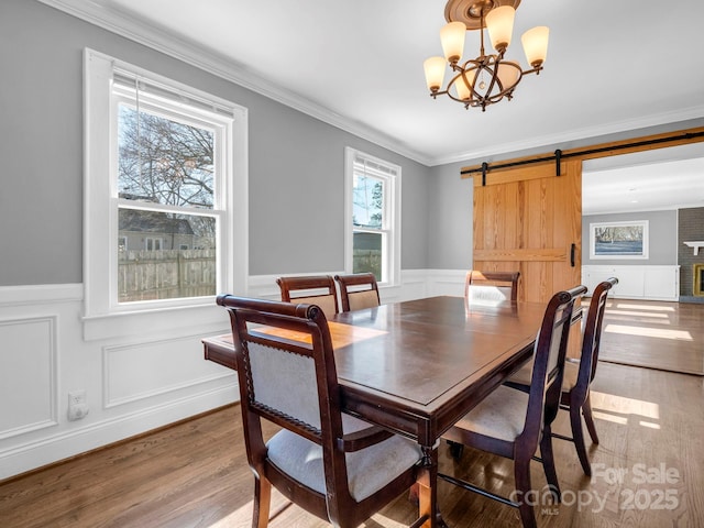 dining area with an inviting chandelier, hardwood / wood-style floors, ornamental molding, and a barn door