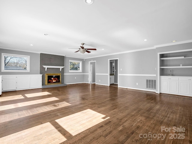 unfurnished living room featuring ceiling fan, ornamental molding, wood-type flooring, and a brick fireplace