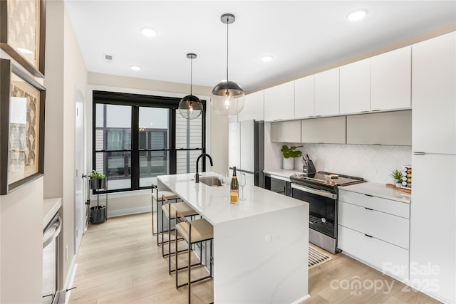 kitchen with pendant lighting, sink, a kitchen island with sink, electric range, and white cabinets