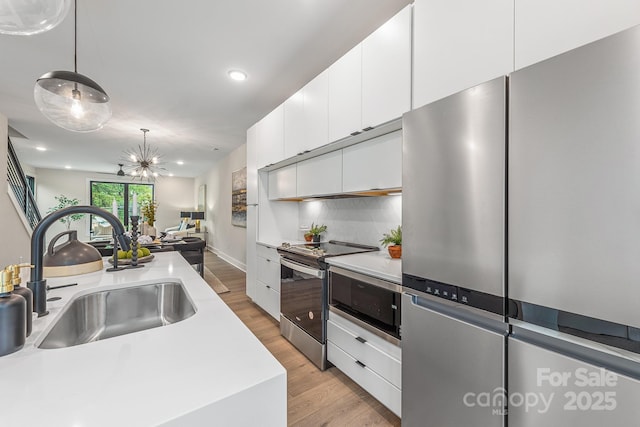 kitchen with modern cabinets, hanging light fixtures, stainless steel appliances, white cabinetry, and a sink