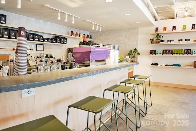 interior space with rail lighting, concrete flooring, and a breakfast bar area