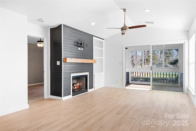 unfurnished living room featuring built in shelves, lofted ceiling, a large fireplace, ceiling fan, and light hardwood / wood-style floors