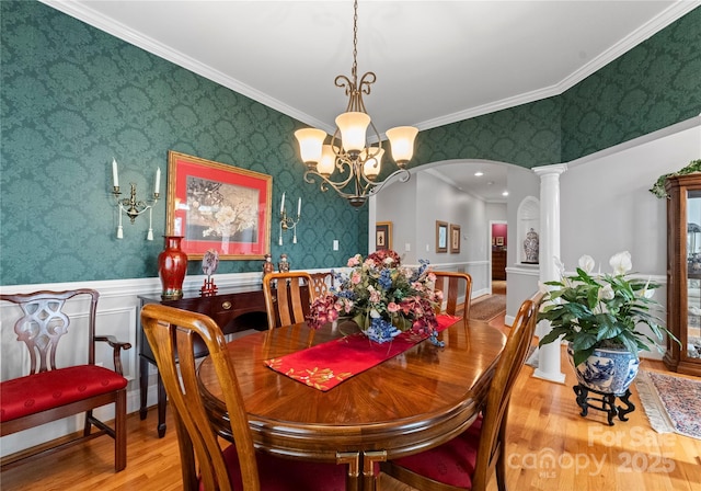 dining room with hardwood / wood-style flooring, crown molding, an inviting chandelier, and ornate columns