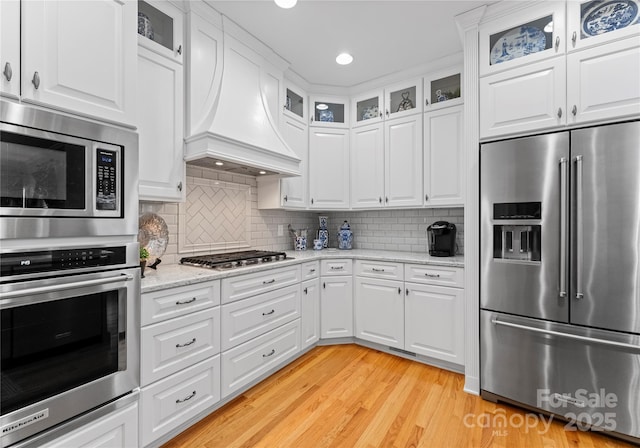 kitchen featuring white cabinetry, stainless steel appliances, light hardwood / wood-style floors, and premium range hood