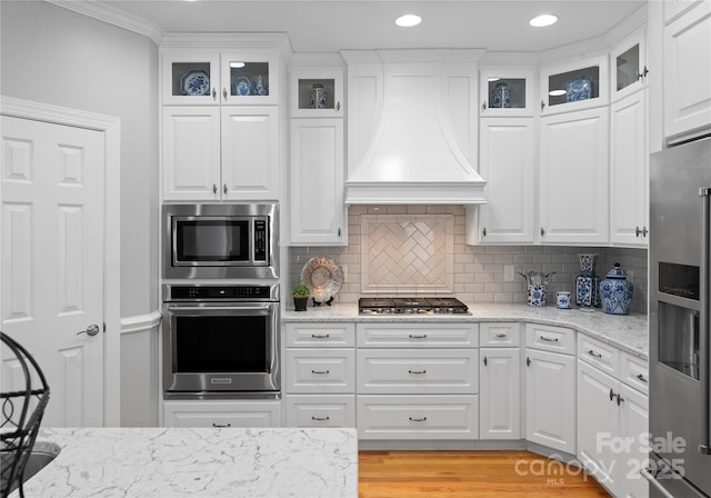 kitchen featuring premium range hood, white cabinetry, appliances with stainless steel finishes, tasteful backsplash, and light stone countertops