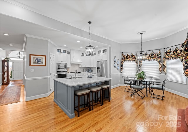 kitchen featuring custom exhaust hood, light stone counters, appliances with stainless steel finishes, a kitchen island with sink, and white cabinets