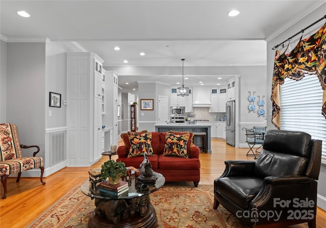 living room featuring crown molding, an inviting chandelier, and light wood-type flooring