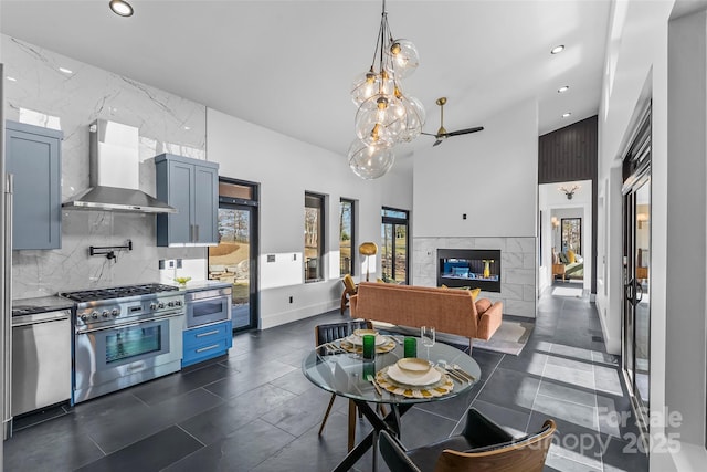 kitchen with wall chimney exhaust hood, blue cabinets, appliances with stainless steel finishes, a fireplace, and decorative backsplash