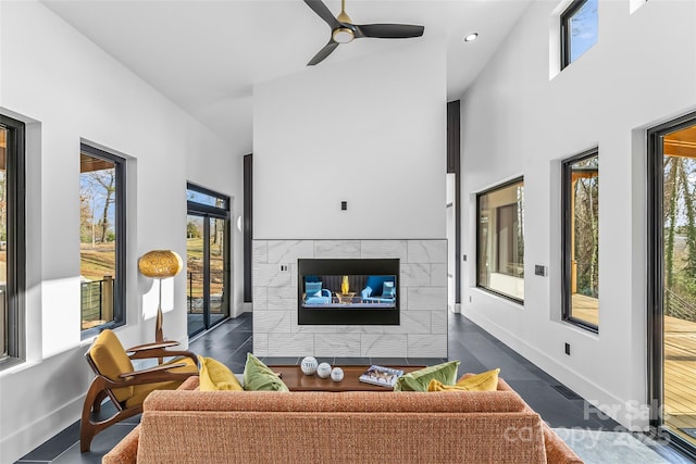 living room with a tiled fireplace, a towering ceiling, plenty of natural light, and ceiling fan