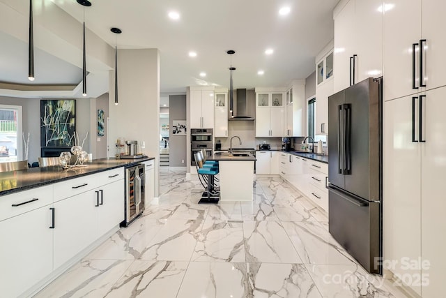 kitchen with hanging light fixtures, appliances with stainless steel finishes, wine cooler, and wall chimney exhaust hood