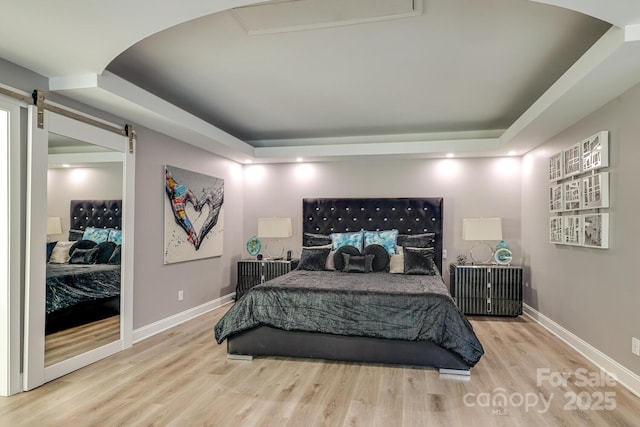 bedroom with a barn door, a raised ceiling, and light hardwood / wood-style flooring