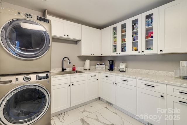 clothes washing area with cabinets, stacked washing maching and dryer, and sink