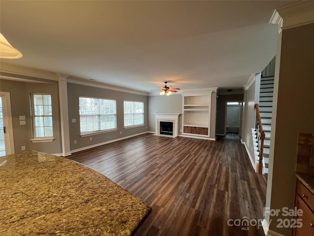 unfurnished living room with baseboards, a ceiling fan, dark wood-style floors, ornamental molding, and a fireplace