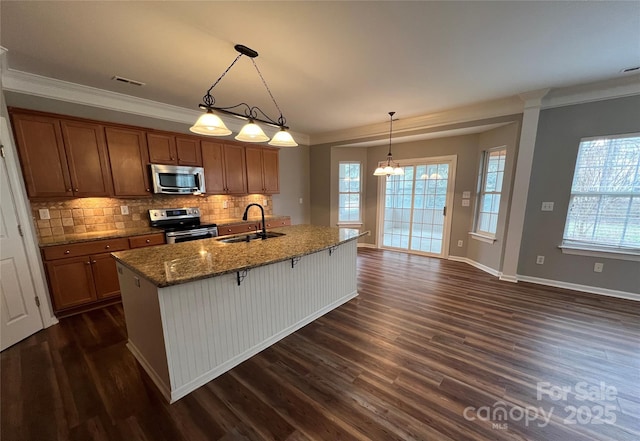 kitchen with stainless steel appliances, a sink, brown cabinetry, a kitchen bar, and pendant lighting