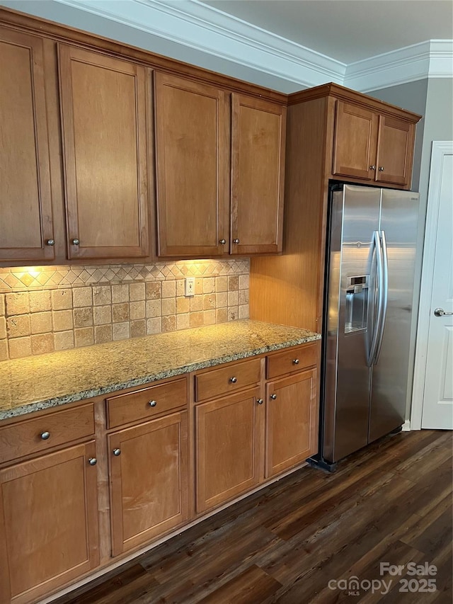 kitchen featuring stainless steel refrigerator with ice dispenser, light stone countertops, brown cabinetry, dark wood finished floors, and crown molding