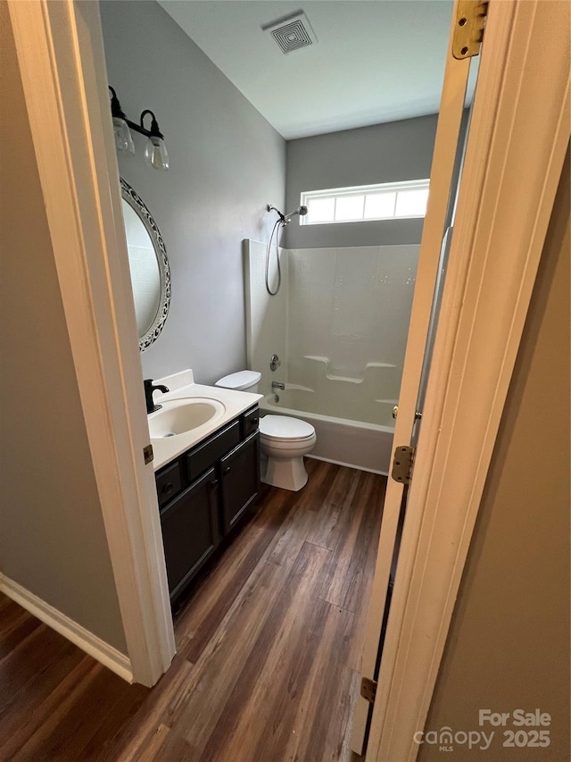 bathroom with toilet, wood finished floors, vanity, visible vents, and washtub / shower combination