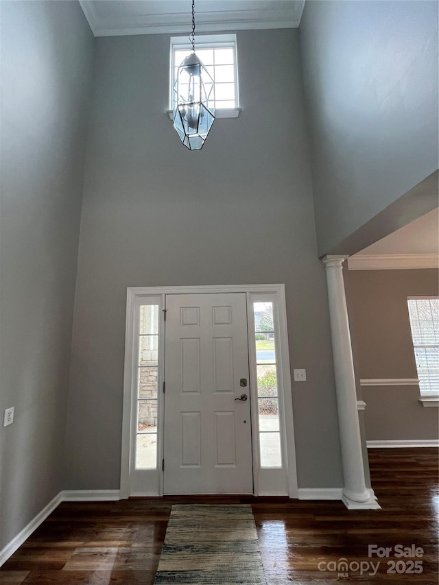 foyer entrance with dark wood-style floors, crown molding, baseboards, and ornate columns