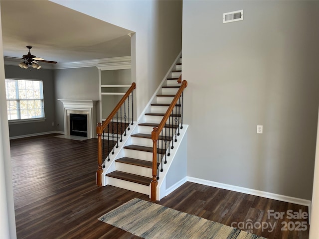 stairs with crown molding, visible vents, a fireplace with flush hearth, wood finished floors, and baseboards