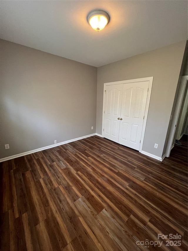 unfurnished bedroom with a closet, baseboards, and dark wood-type flooring