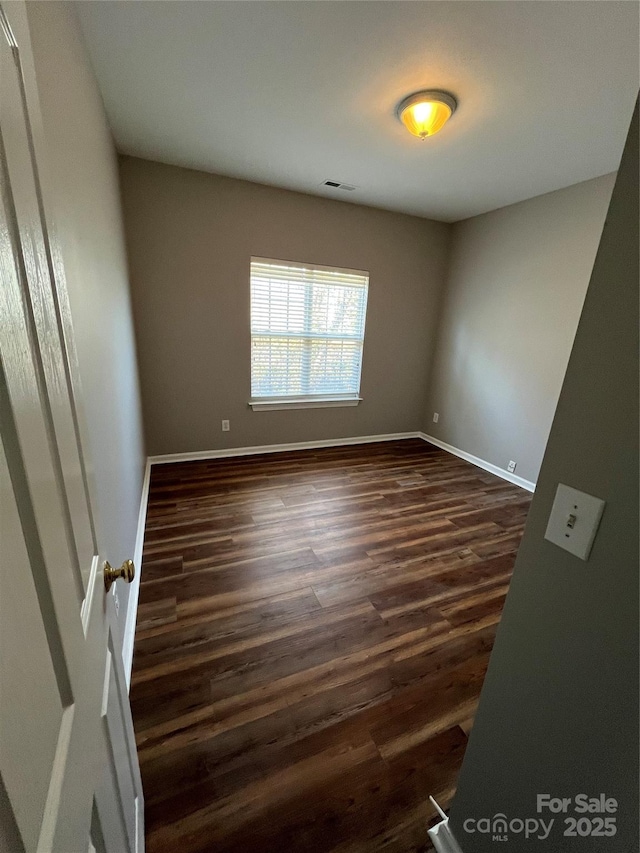 unfurnished room featuring dark wood-style flooring, visible vents, and baseboards