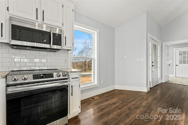 kitchen featuring appliances with stainless steel finishes, white cabinetry, dark hardwood / wood-style flooring, decorative backsplash, and light stone counters