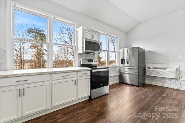 kitchen with appliances with stainless steel finishes, dark hardwood / wood-style floors, white cabinets, vaulted ceiling, and an AC wall unit