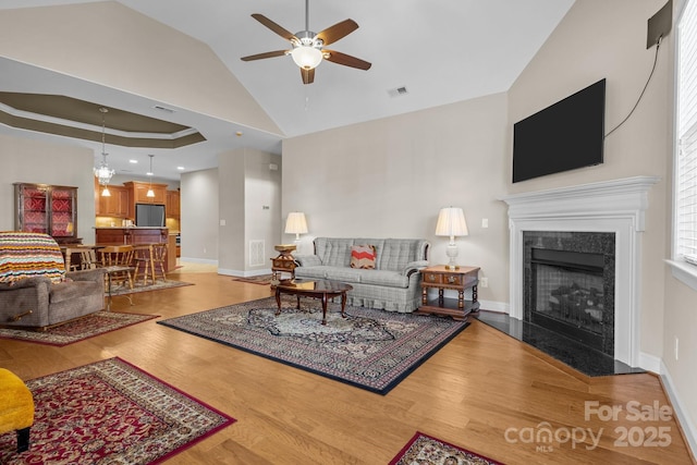 living room featuring high vaulted ceiling, a raised ceiling, ceiling fan, a fireplace, and hardwood / wood-style floors