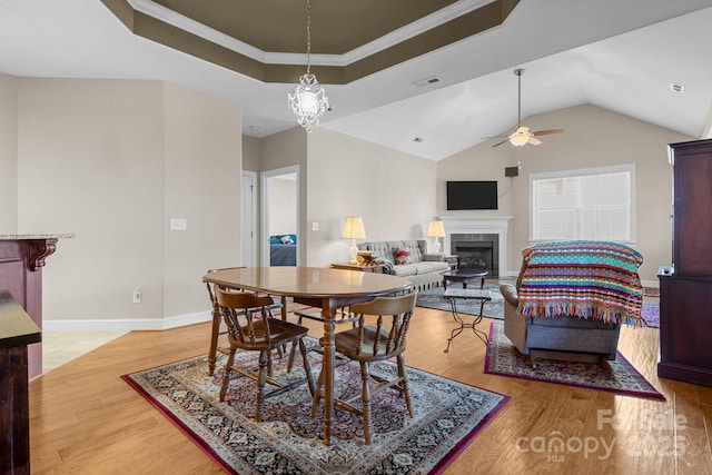 dining room with ceiling fan with notable chandelier, a fireplace, wood-type flooring, ornamental molding, and a tray ceiling