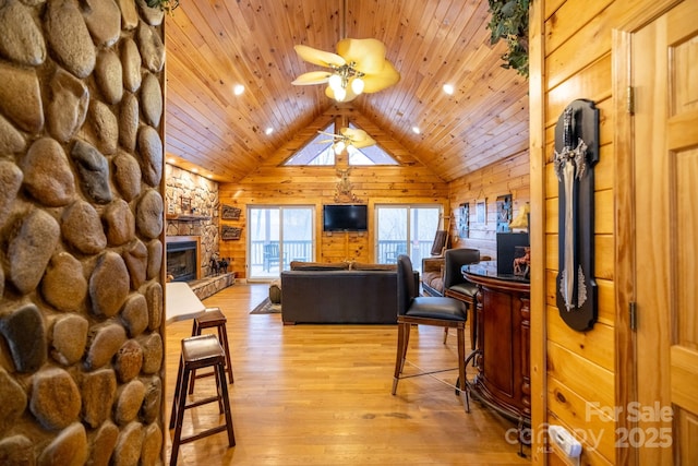 living room with wood ceiling, wooden walls, light hardwood / wood-style floors, a stone fireplace, and vaulted ceiling