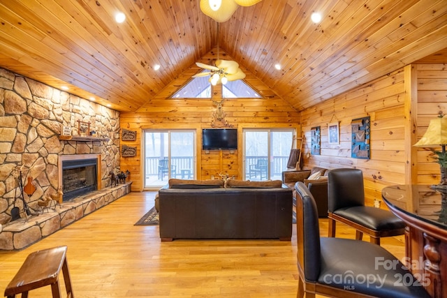 living room with vaulted ceiling, a fireplace, light wood-type flooring, and wood walls