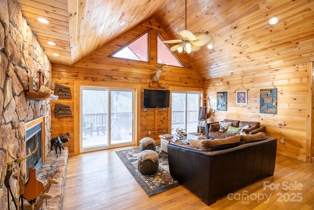 living room with a stone fireplace, wooden walls, and light wood-type flooring