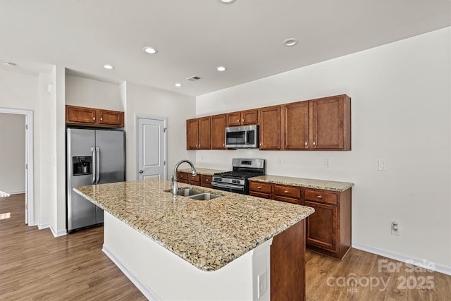 kitchen with stainless steel appliances, an island with sink, sink, and light stone counters