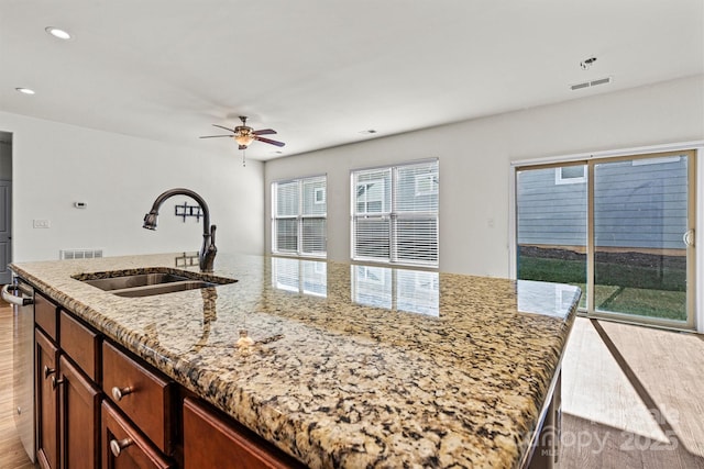 kitchen with an island with sink, light stone countertops, sink, and light wood-type flooring