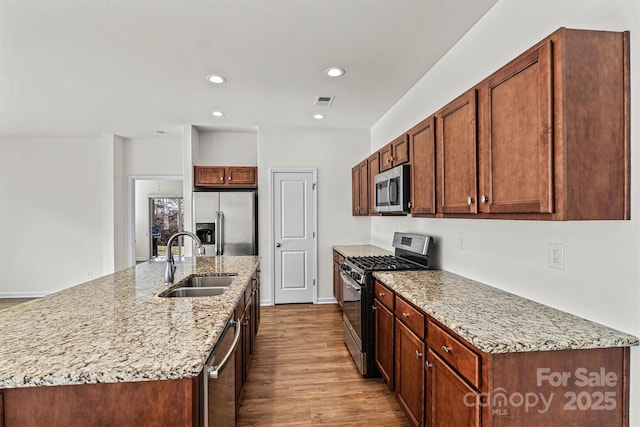 kitchen with sink, stainless steel appliances, light stone countertops, a center island with sink, and light wood-type flooring