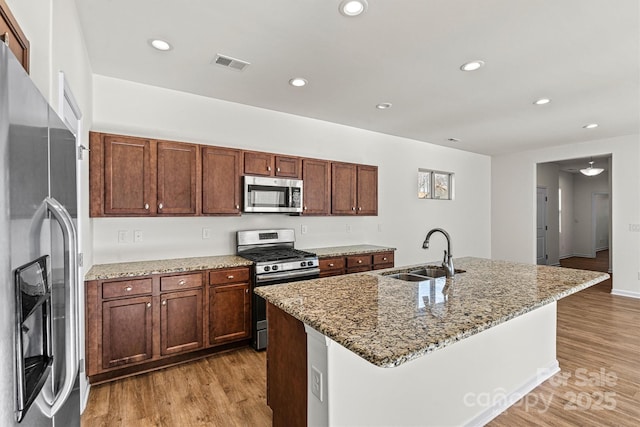 kitchen with sink, light stone counters, a center island with sink, stainless steel appliances, and light hardwood / wood-style floors